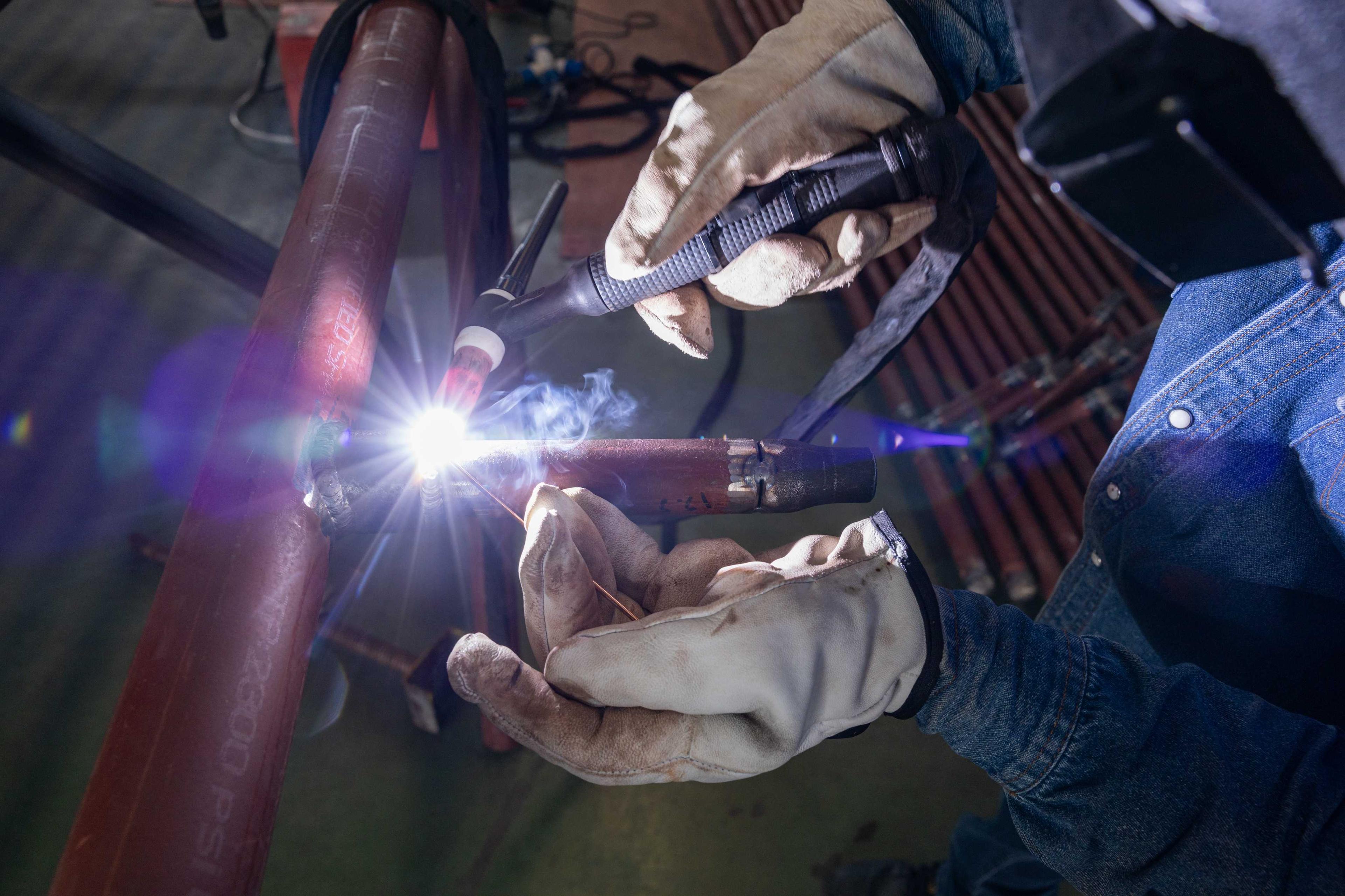 Welder performing TIG welding on metal pipe