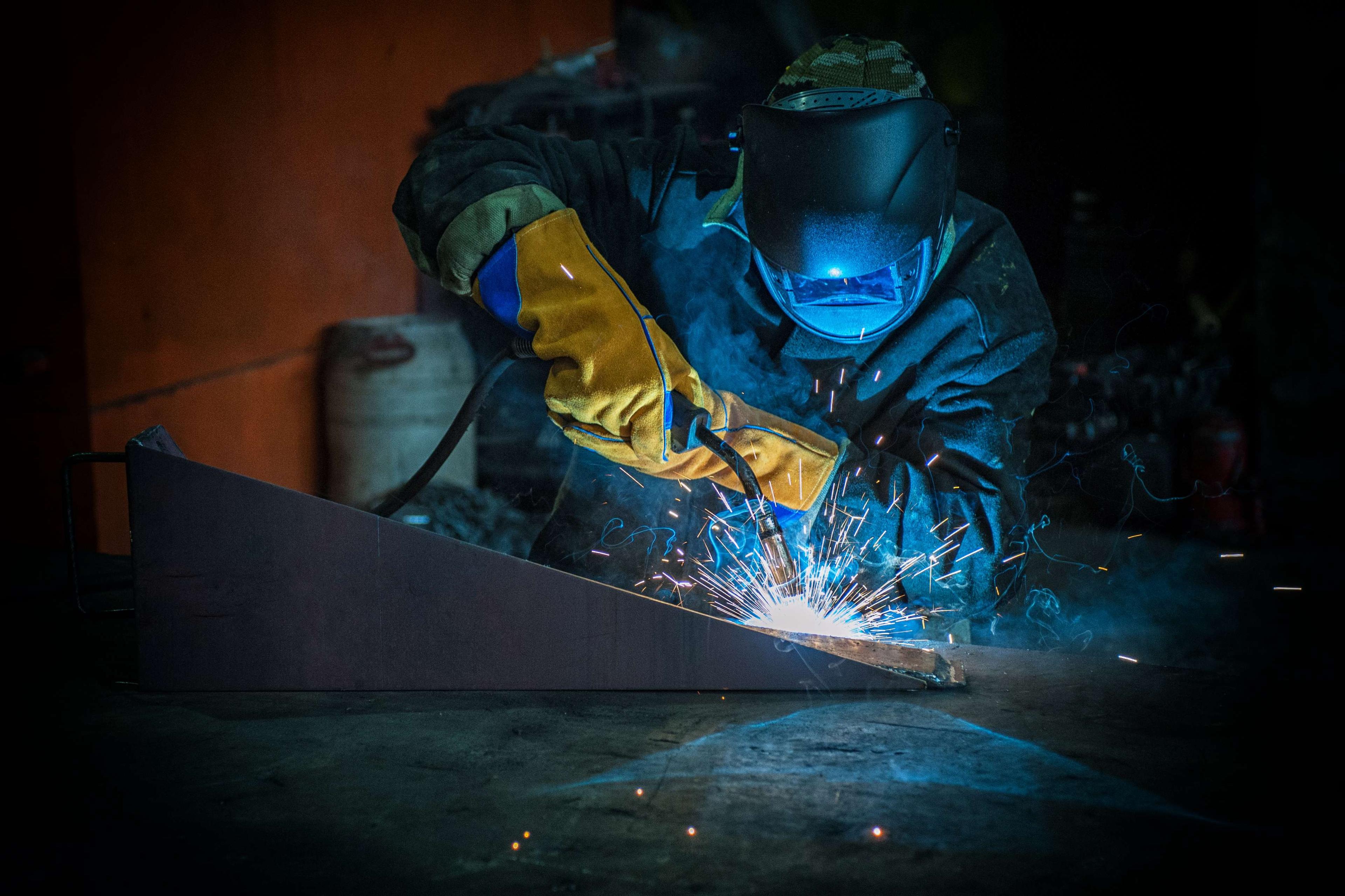 Worker welding metal with sparks at factory